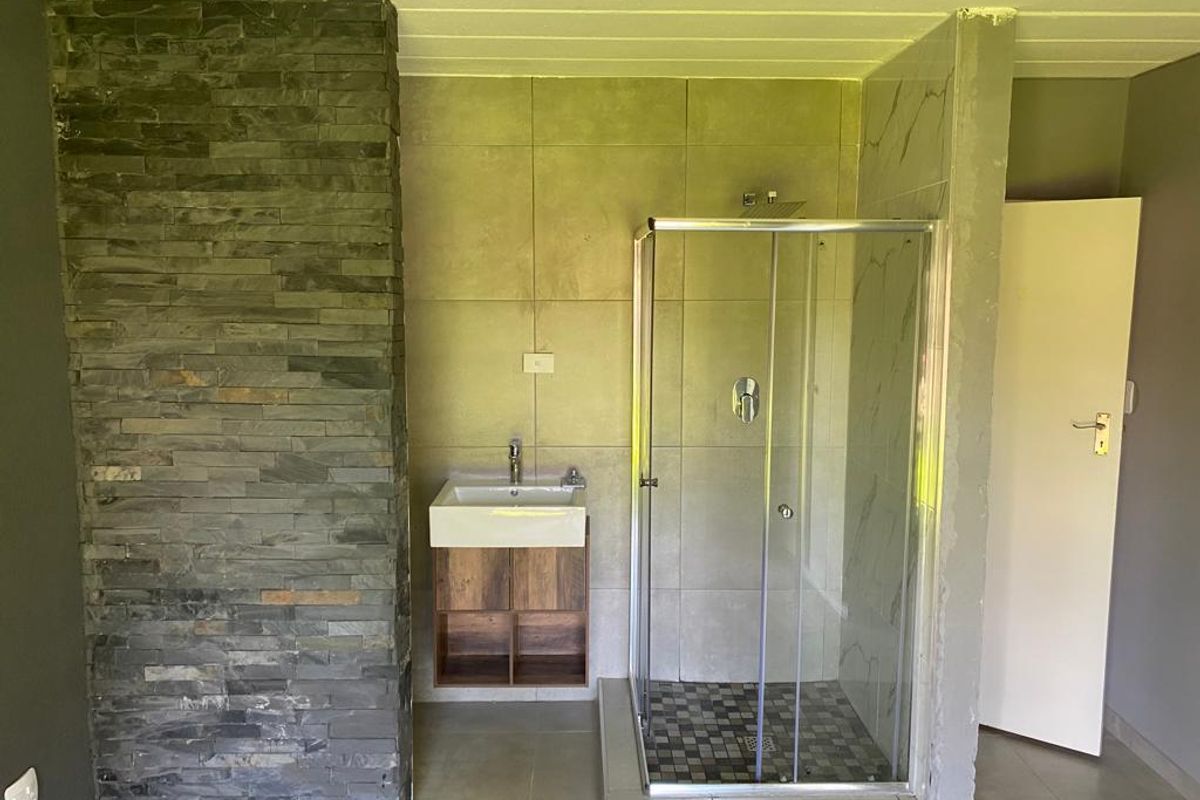 A modern bathroom featuring a glass-enclosed shower, a floating vanity with a basin, and a decorative stone-clad feature wall.