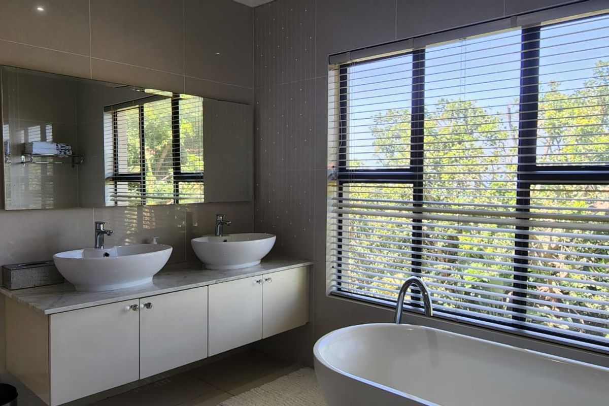 Modern bathroom featuring a floating double vanity with vessel sinks, a large wall-mounted mirror, and a freestanding bathtub positioned by a window.
