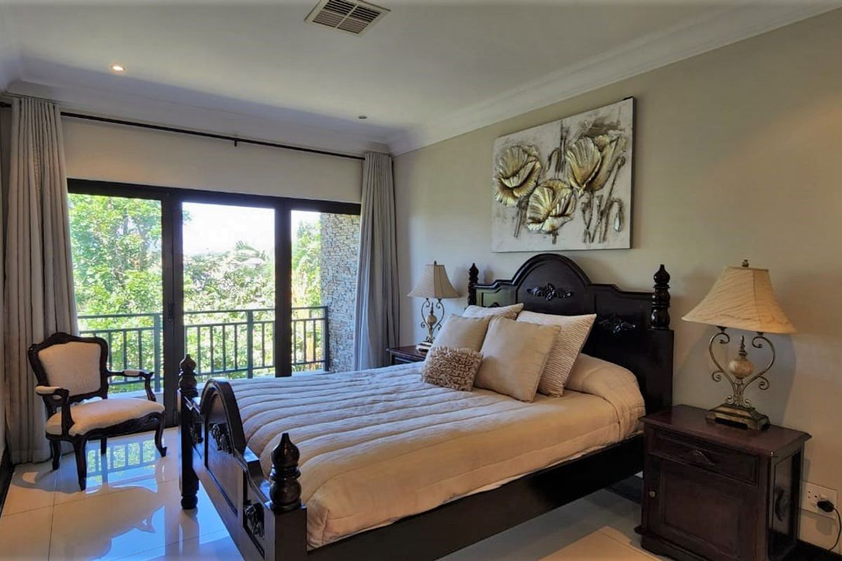 A well-maintained bedroom featuring large sliding glass doors that open onto a private balcony with lush green views.