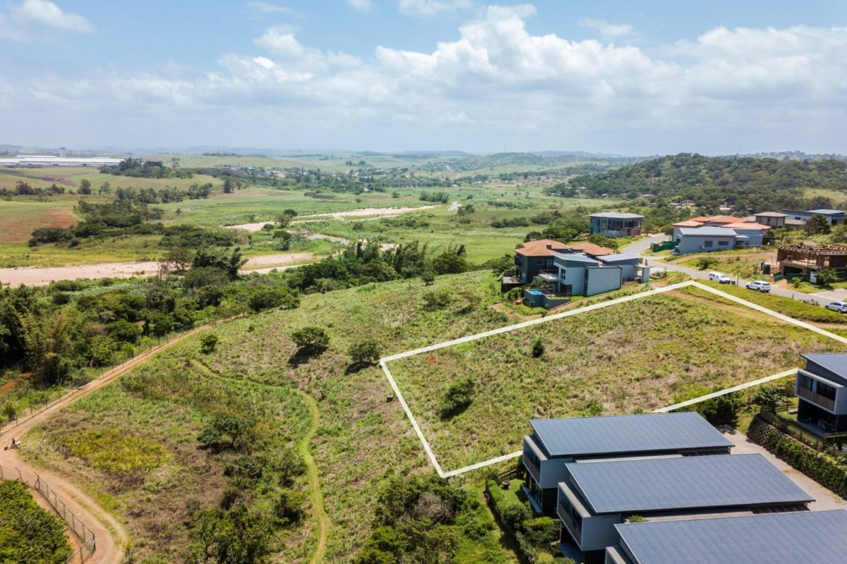 An aerial view of a vacant residential plot with clear boundary markings, situated in a scenic estate with surrounding natural landscape.