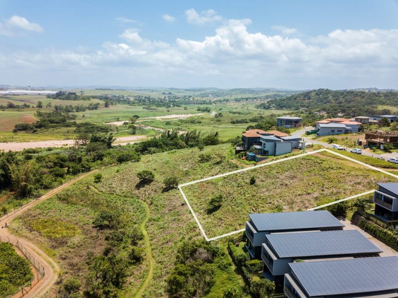 An aerial view of a vacant residential plot with clear boundary markings, situated in a scenic estate with surrounding natural landscape.