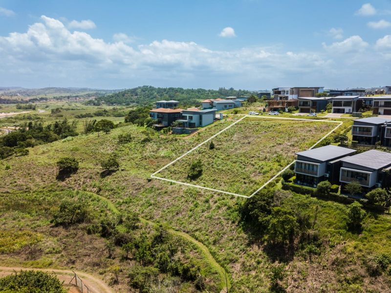 An aerial view of a vacant residential plot situated on a hillside within a developed estate, offering potential for custom home construction.