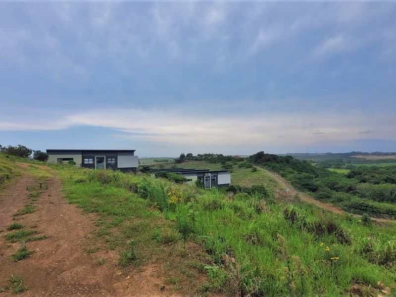 An elevated view of a residential plot featuring unpaved access tracks, modern dwellings, and surrounding natural landscape.