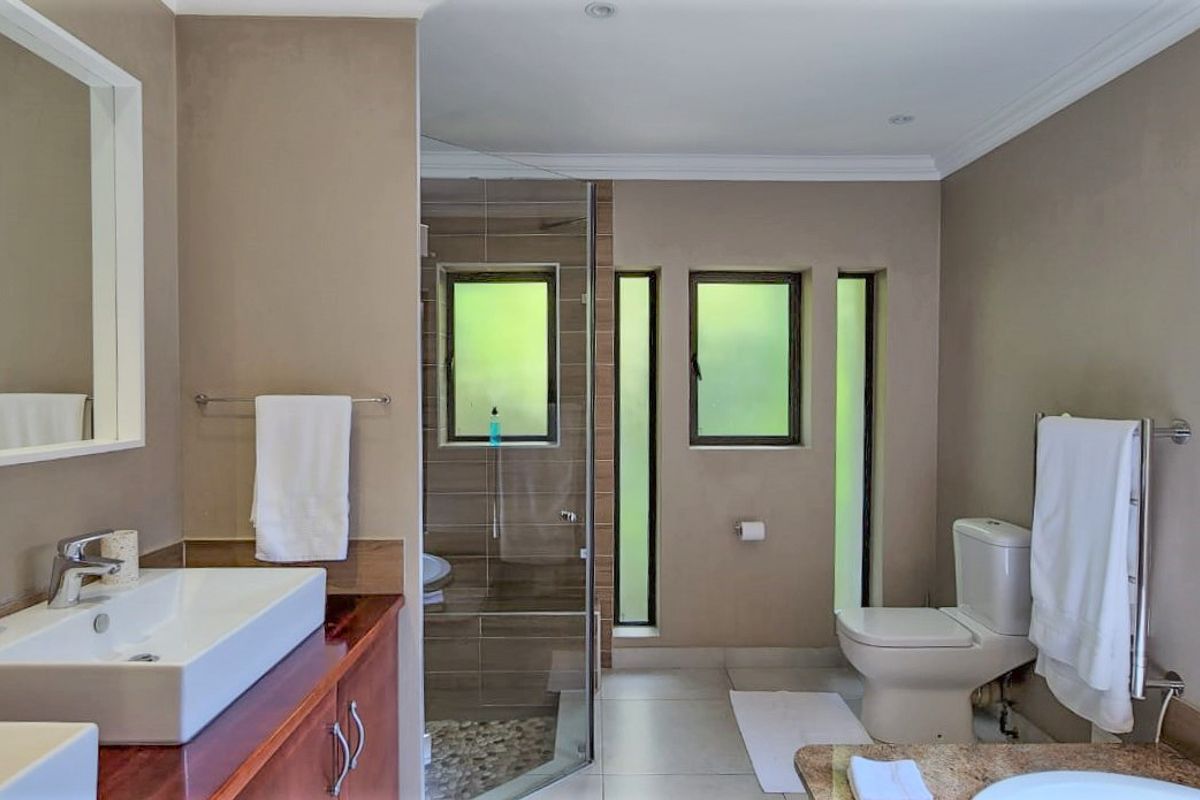 A modern bathroom featuring a glass-enclosed shower, dual vanity with vessel sinks, and a toilet, finished with neutral wall tones and tiled flooring.