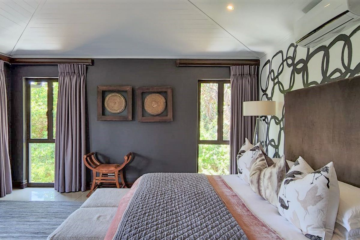 A well-maintained bedroom featuring dark accent walls, large windows with curtains, recessed ceiling lighting, and a wall-mounted air conditioning unit.