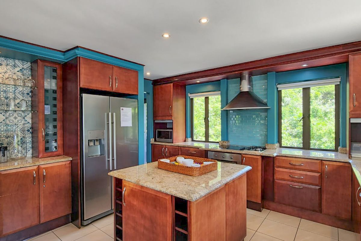 A spacious kitchen featuring cherry wood cabinetry, granite countertops, a central island, stainless steel appliances, and decorative tiled backsplash.