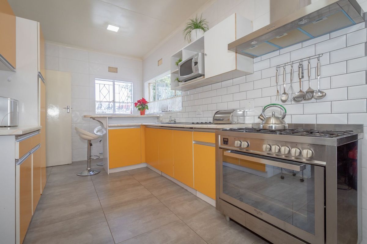A functional kitchen featuring bright orange cabinetry, a gas stove with extractor fan, subway tile backsplash, and a convenient breakfast bar area.
