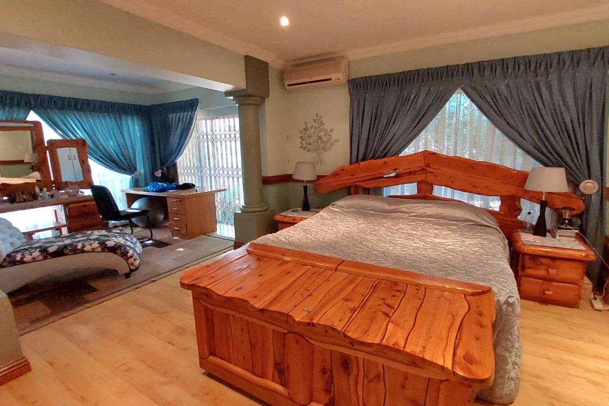 Spacious bedroom featuring laminate flooring, a split-system air conditioning unit, and an integrated seating or study area with decorative columns.