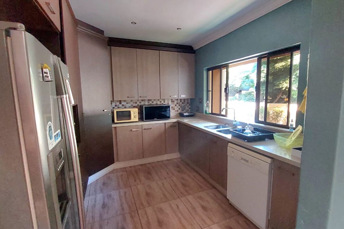 A functional kitchen featuring wood-look cabinetry, tiled flooring, a double sink, and a window overlooking the garden area.