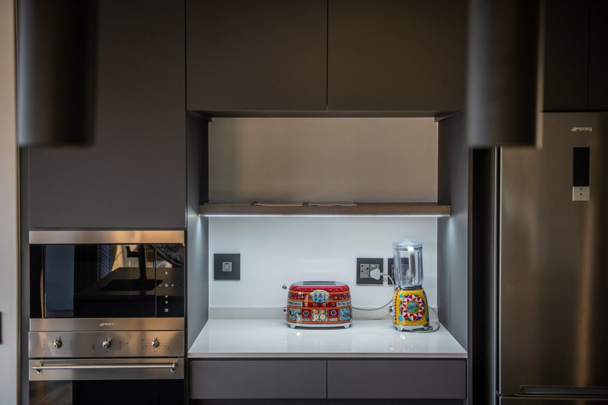 Modern kitchen featuring dark cabinetry, integrated oven, stone countertops, and under-cabinet LED lighting.