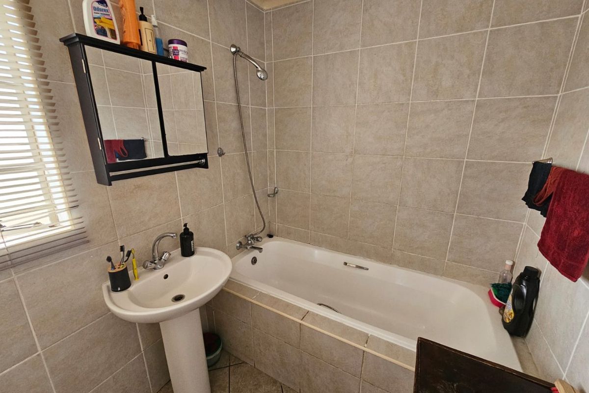 A functional bathroom featuring a pedestal basin, a bathtub with a shower mixer, and neutral wall tiling.