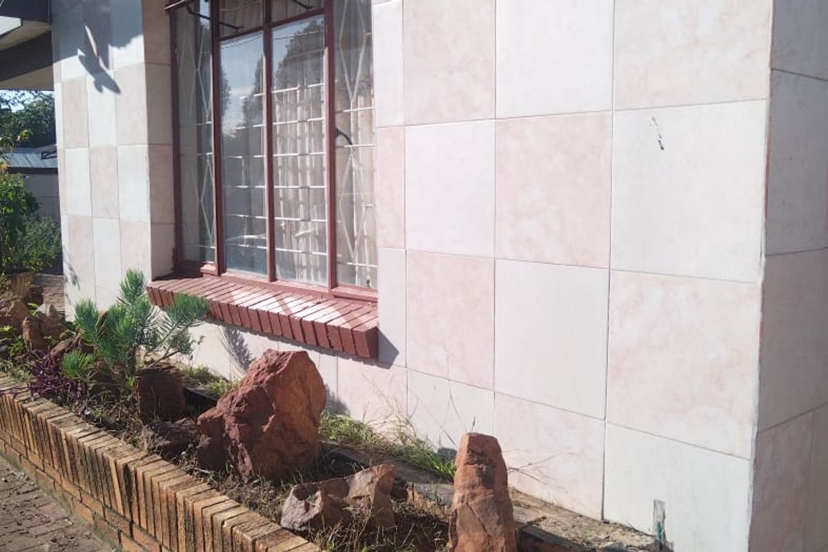 Exterior view of the property featuring tiled wall cladding, a brick planter box, and metal security bars on the window.