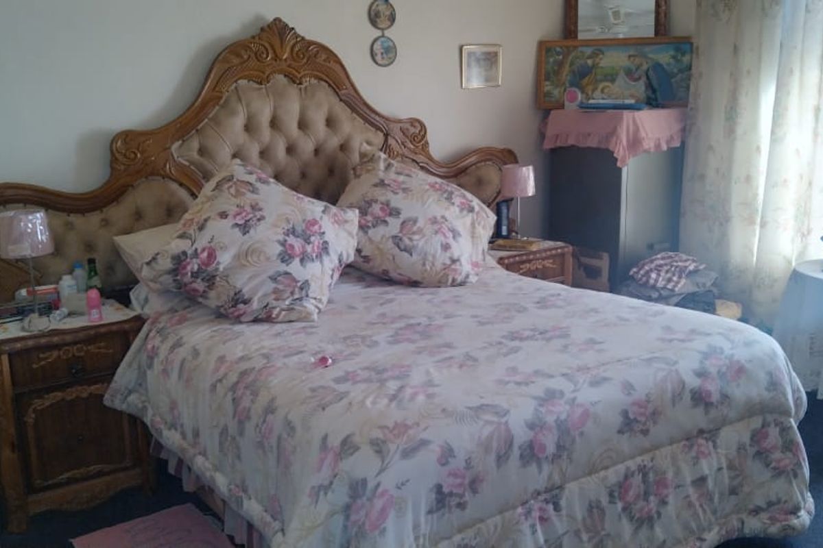 A bedroom featuring a large ornate headboard, carpeted flooring, and natural light from the window.
