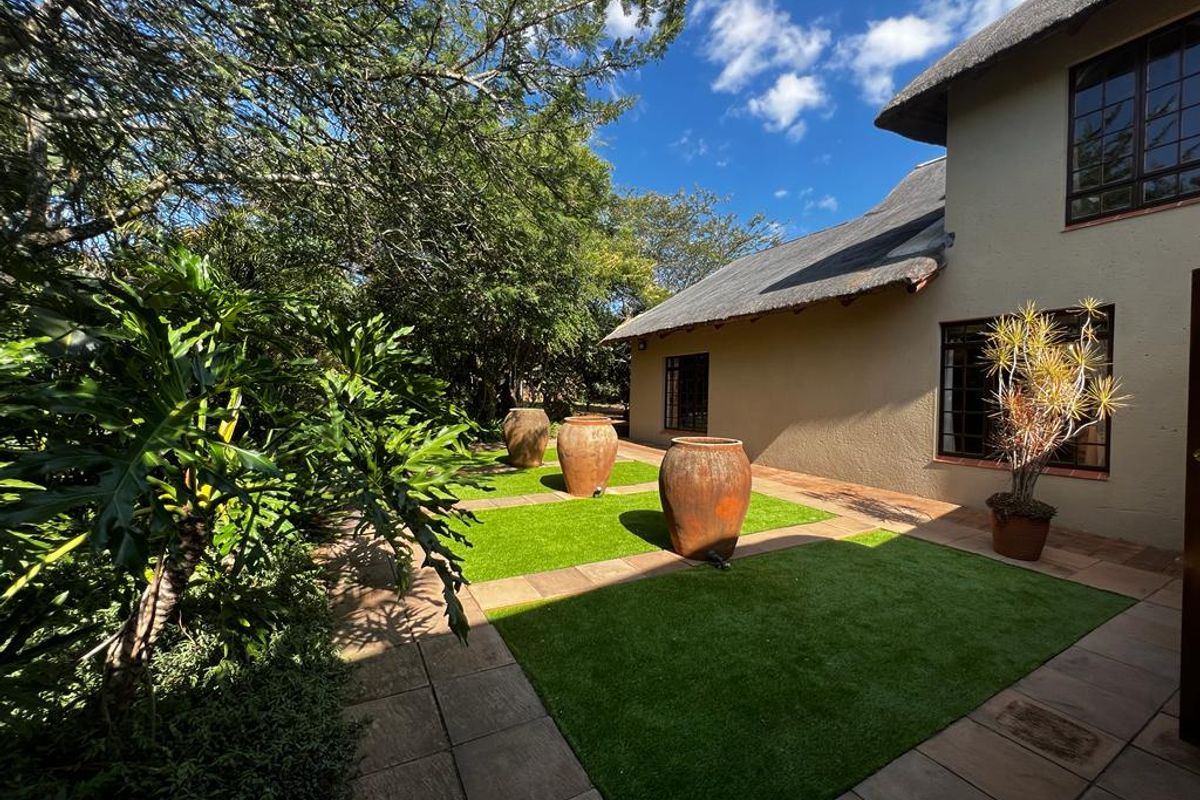 A well-maintained rear garden area featuring paved pathways, artificial grass sections, and a thatched roof house exterior.