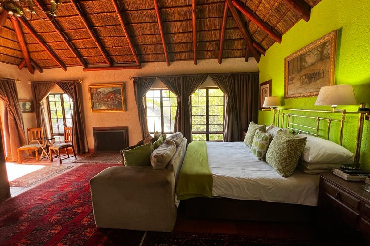 Spacious bedroom featuring a high vaulted thatched ceiling, exposed timber beams, a built-in fireplace, and large windows providing natural light.