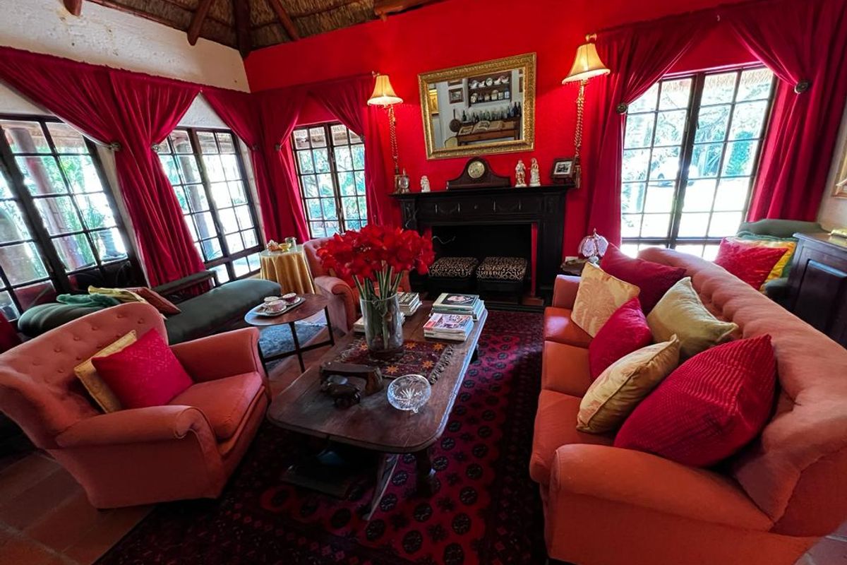 A cozy living room featuring a traditional fireplace, exposed thatch ceiling, and multiple windows providing natural light.