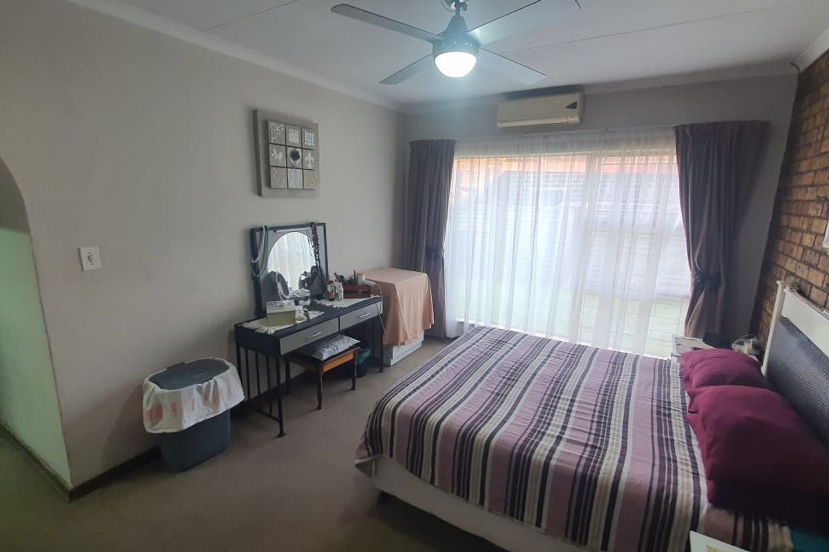 A bedroom featuring a brick feature wall, ceiling fan, and wall-mounted air conditioning unit, with large windows providing natural light.