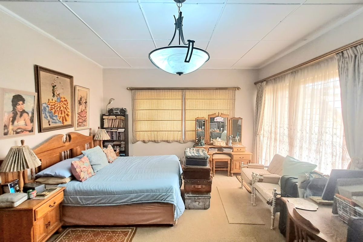 Spacious bedroom featuring large windows with natural light, neutral wall tones, and a central pendant light fixture.