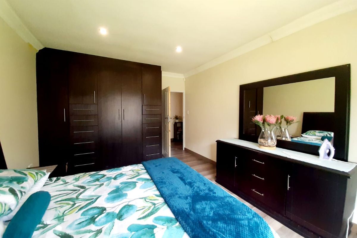 A well-maintained bedroom featuring dark wood built-in cupboards and matching dresser with mirror, finished with neutral walls and recessed ceiling lighting.