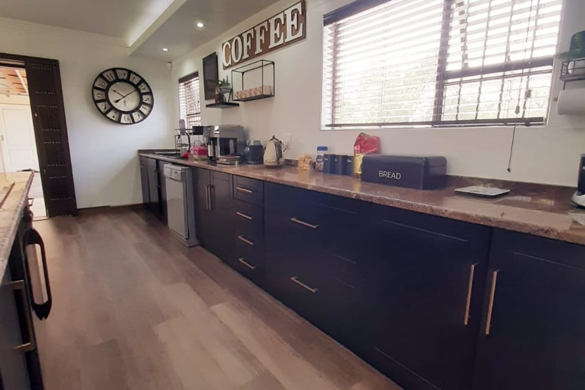A modern kitchen featuring dark cabinetry, stone countertops, recessed lighting, and wood-look flooring, offering a clean and functional workspace.