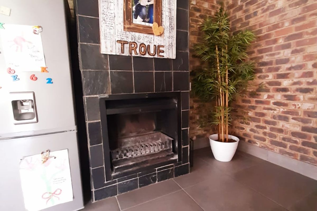 A cozy living area featuring a built-in fireplace with dark slate tiling, exposed brick walls, and large format floor tiles.