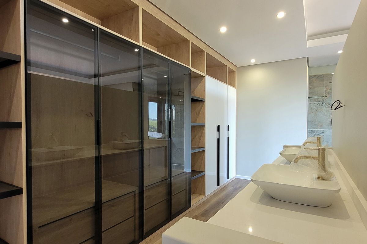 Modern bathroom featuring a double vanity with vessel sinks, gold-tone fixtures, and extensive built-in cabinetry with glass-fronted wardrobe storage.