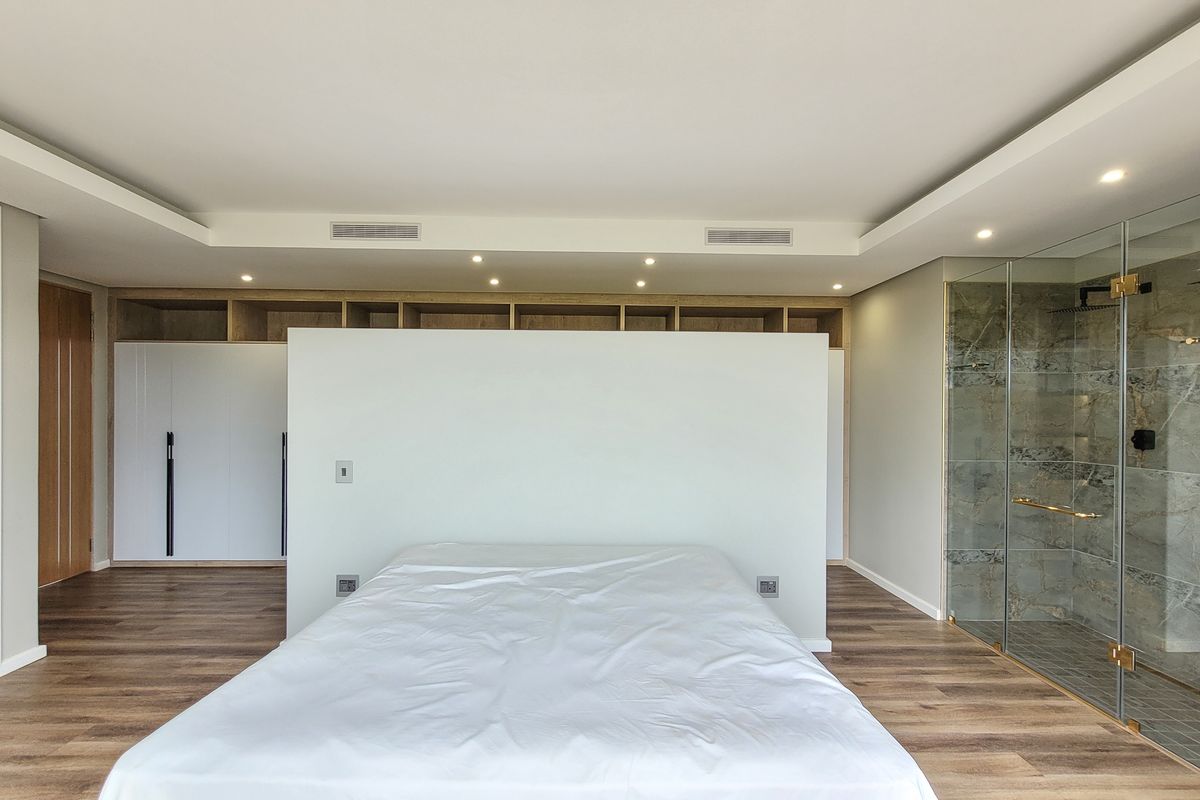 Modern open-plan bedroom featuring a central partition wall, integrated timber cabinetry, and an en-suite glass-enclosed shower with stone-look tiling.