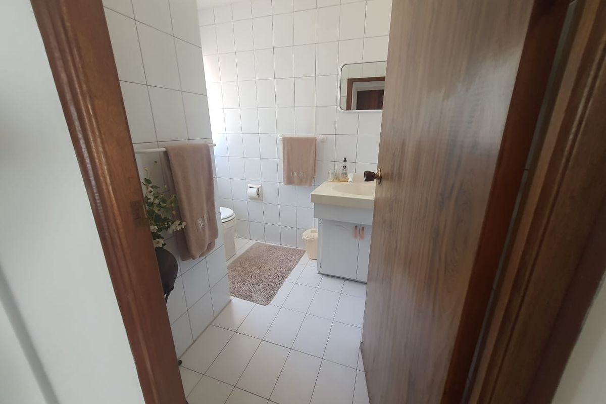 A functional bathroom featuring white wall and floor tiles, a built-in vanity unit with basin, and a standard toilet.