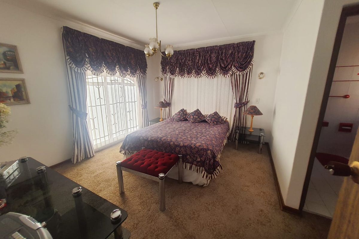 A spacious bedroom featuring carpeted flooring, a security gate, and classic window treatments, offering a comfortable and functional living space.