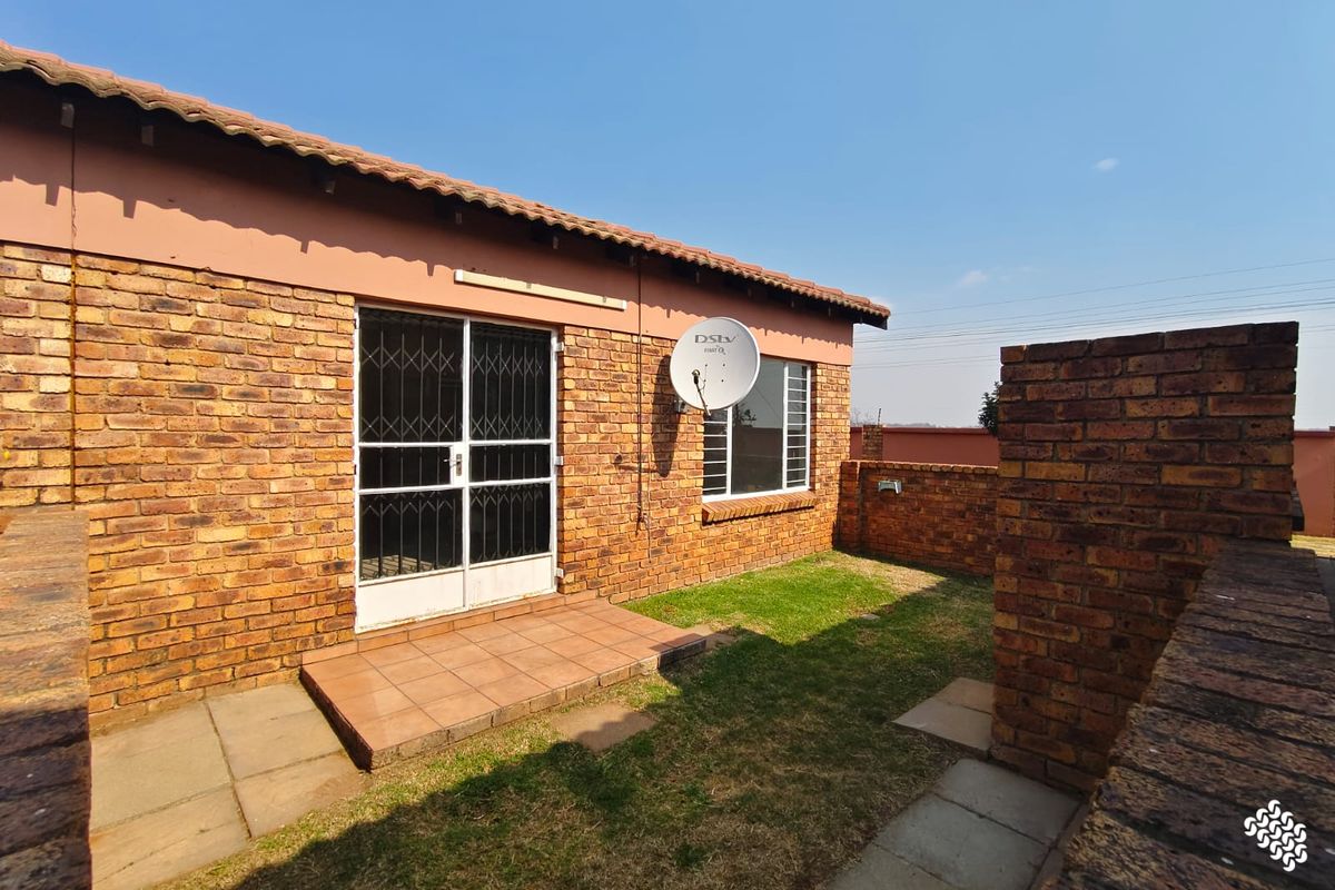 Rear exterior view of the townhouse featuring a face brick facade, tiled roof, small paved patio area, and a private garden space.