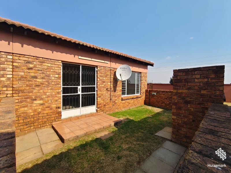 Rear exterior view of the townhouse featuring a face brick facade, tiled roof, small paved patio area, and a private garden space.