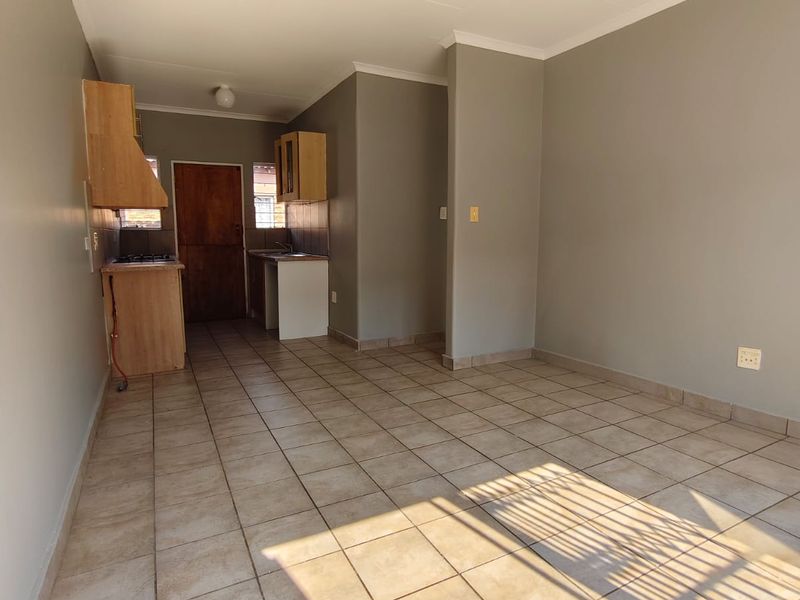 An open-plan living and kitchen area featuring neutral wall tones, tiled flooring, and basic built-in kitchen cabinetry.