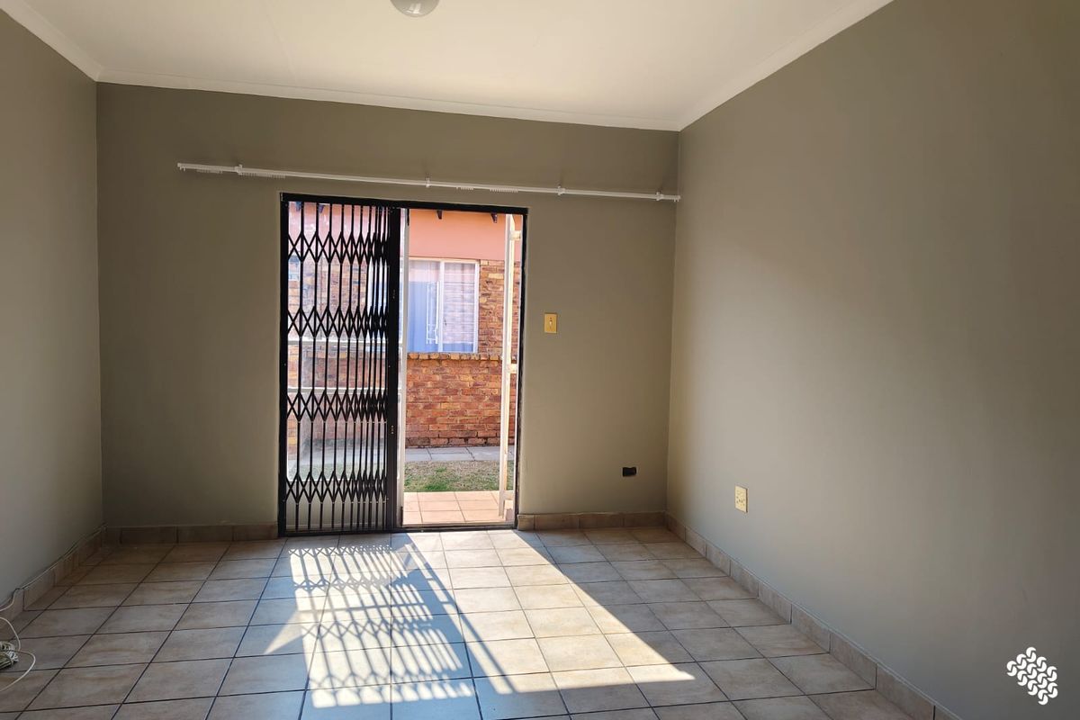 An empty living room featuring tiled flooring and a sliding door with a security gate leading to the exterior.
