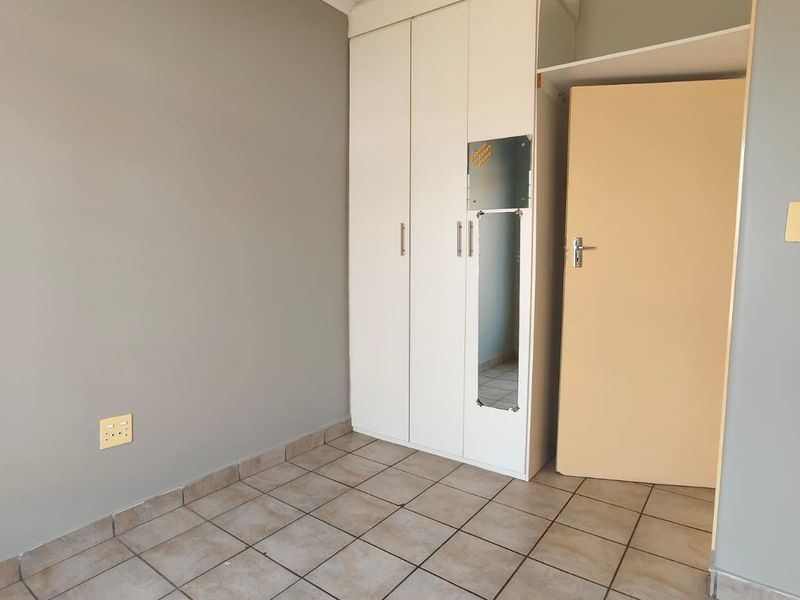 A clean, empty bedroom featuring neutral grey walls, tiled flooring, and a white built-in wardrobe with a mirrored panel.
