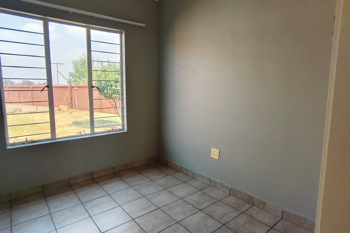 A clean, empty bedroom featuring neutral grey walls, tiled flooring, and large windows with security bars, offering a blank canvas for personalization.
