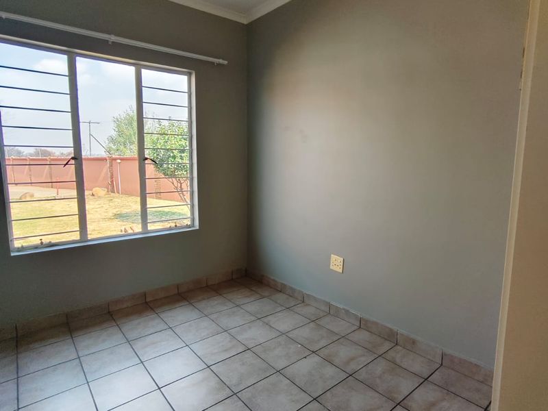 A clean, empty bedroom featuring neutral grey walls, tiled flooring, and large windows with security bars, offering a blank canvas for personalization.