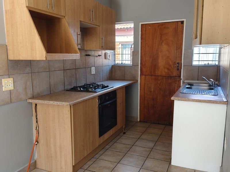 A functional kitchen featuring built-in wooden cabinetry, a gas hob, an integrated oven, and tiled flooring with a neutral backsplash.