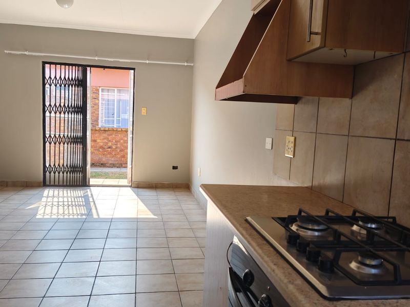 Open plan kitchen and living area featuring tiled flooring, built-in cabinetry, gas hob, and direct access to the rear exterior through a security gate.