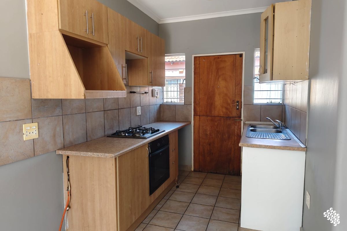 A functional kitchen featuring built-in wooden cabinetry, a gas hob, an integrated oven, and a stainless steel sink with tiled splashbacks.