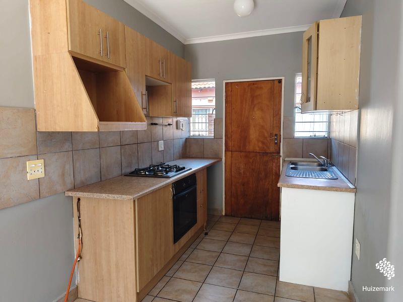 A functional kitchen featuring built-in wooden cabinetry, a gas hob, an integrated oven, and a stainless steel sink with tiled splashbacks.