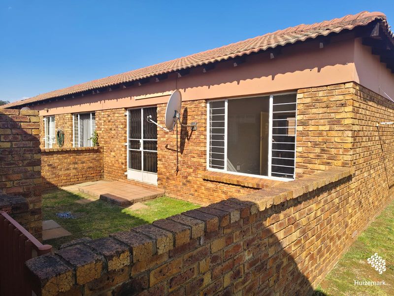 Rear view of a face brick townhouse featuring a small private garden, paved patio area, and secure window bars.