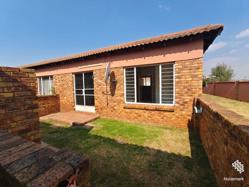 Rear view of a face brick townhouse featuring a small private garden, paved patio area, and secure window bars.