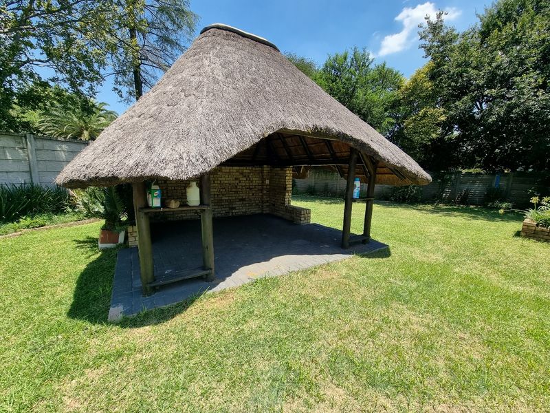 Outdoor thatched lapa area featuring a brick-paved floor and timber support structure, situated within a private garden setting.