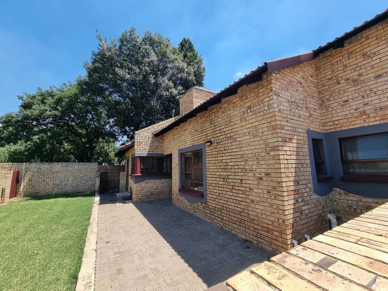 Rear view of the townhouse featuring a face brick facade, paved patio area, and a well-maintained lawn with perimeter boundary walling.