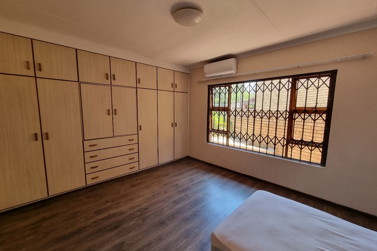 A well-maintained bedroom featuring extensive built-in cabinetry, laminate flooring, and an air conditioning unit, providing ample storage and climate control.
