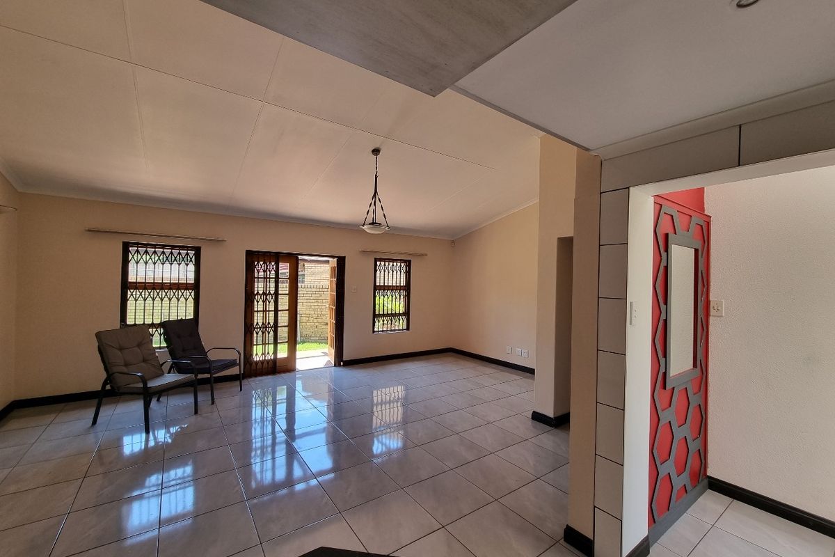 Spacious open-plan living area featuring neutral tiled flooring, decorative wall accents, and direct access to the outdoor space through security-fitted doors.