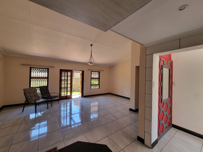 Spacious open-plan living area featuring neutral tiled flooring, decorative wall accents, and direct access to the outdoor space through security-fitted doors.