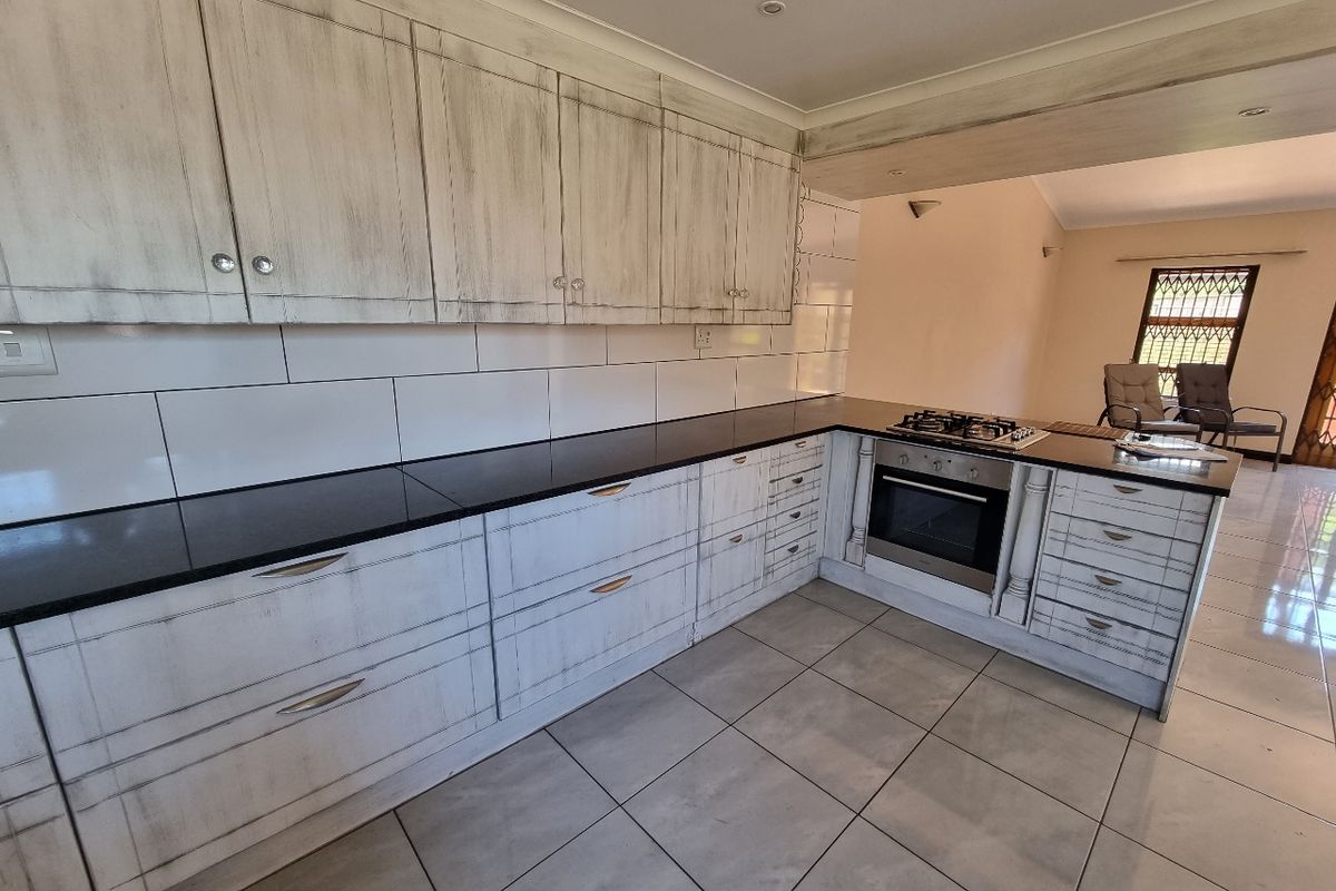 A functional kitchen featuring distressed-finish cabinetry, black granite countertops, a built-in oven, and a gas hob, with neutral tiled flooring throughout.
