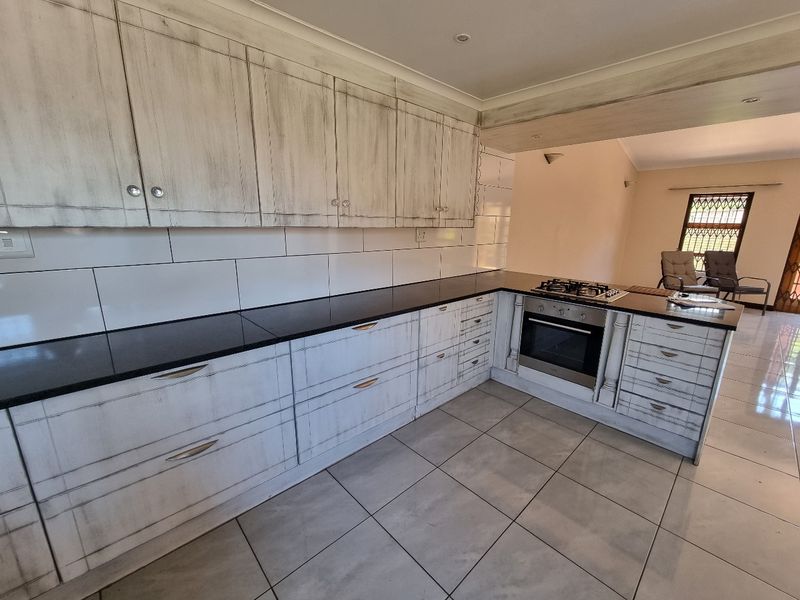 A functional kitchen featuring distressed-finish cabinetry, black granite countertops, a built-in oven, and a gas hob, with neutral tiled flooring throughout.