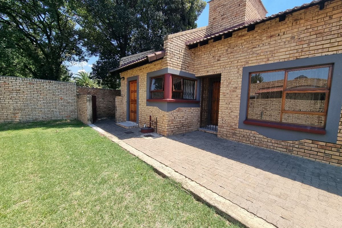Rear view of the townhouse featuring a face brick facade, a paved patio area, and a private garden with a surrounding boundary wall.